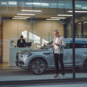 Mann übergibt Autoschlüssel vor einer modernen Bankfiliale mit einem deutschen Mittelklassewagen.Mann übergibt Autoschlüssel vor einer modernen Bankfiliale mit einem deutschen Mittelklassewagen.Mann übergibt Autoschlüssel vor einer modernen Bankfiliale mit einem deutschen Mittelklassewagen.